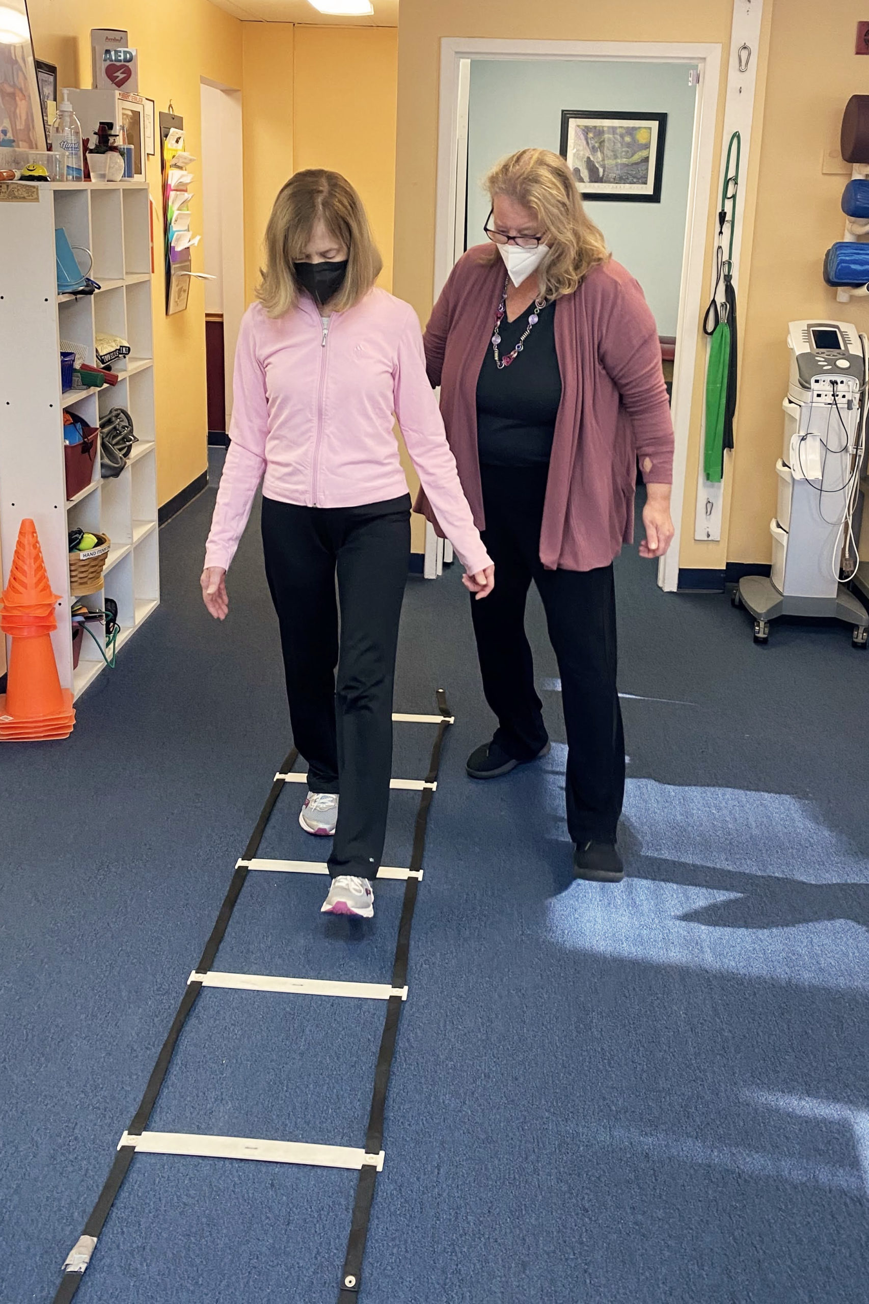 a therapist guiding a patient walking over a ladder on the floor